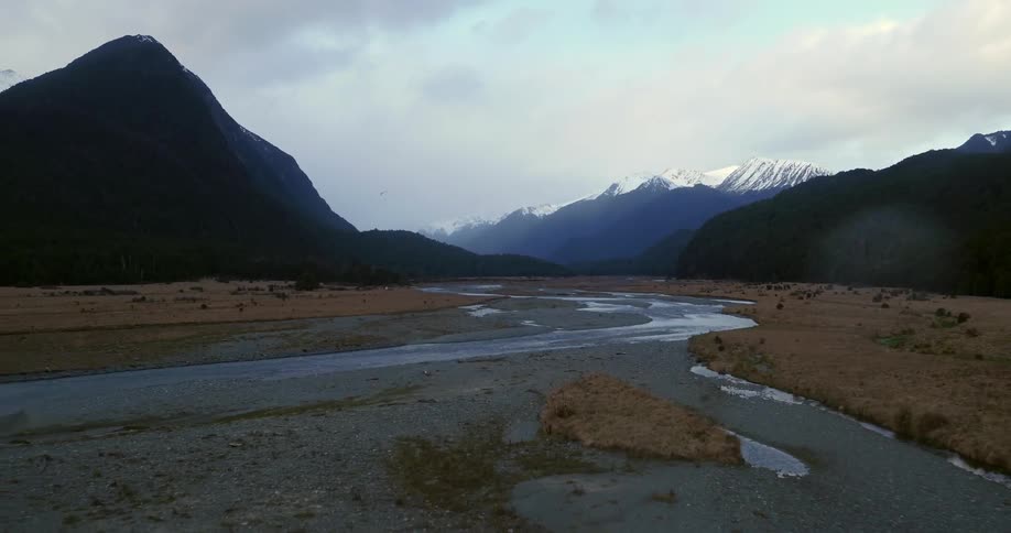 A bird flies over a riverbed in a mountain valley