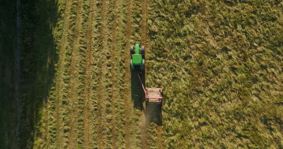 A tractor is cutting grass in a field with the sun shining from a drone looking down