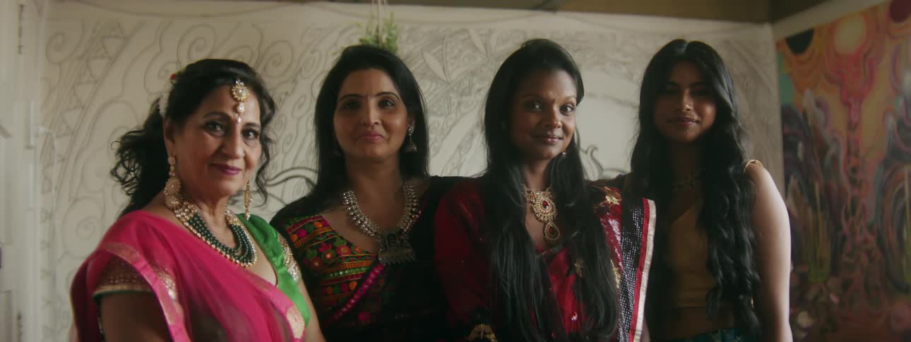 A group of indian women are dressed up and standing together smiling