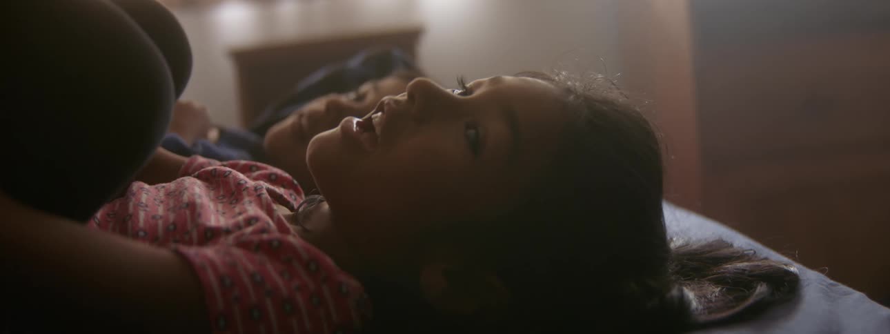 Two girls lying side by side on a bed talking with legs raised and hands under knees