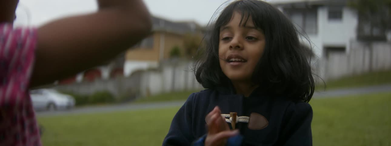 A girl mimics the actions of another girl as they play together outdoors during the day