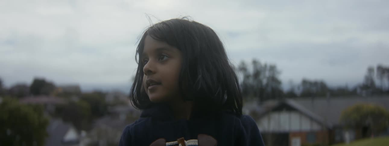 Girl with dark hair and navy blue pullover looks around in playground