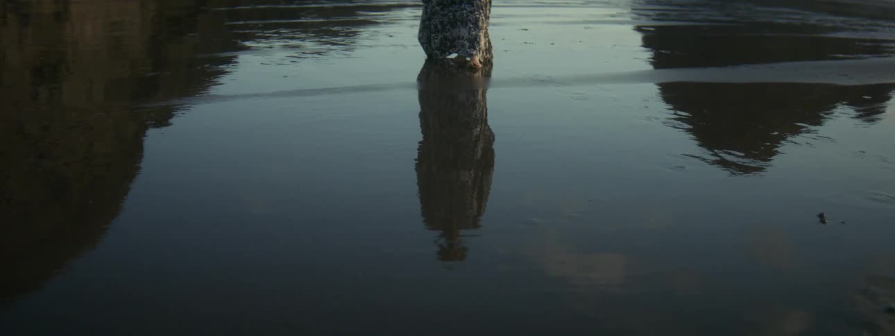 Elderly woman with long dress walks on wet sand on the coast