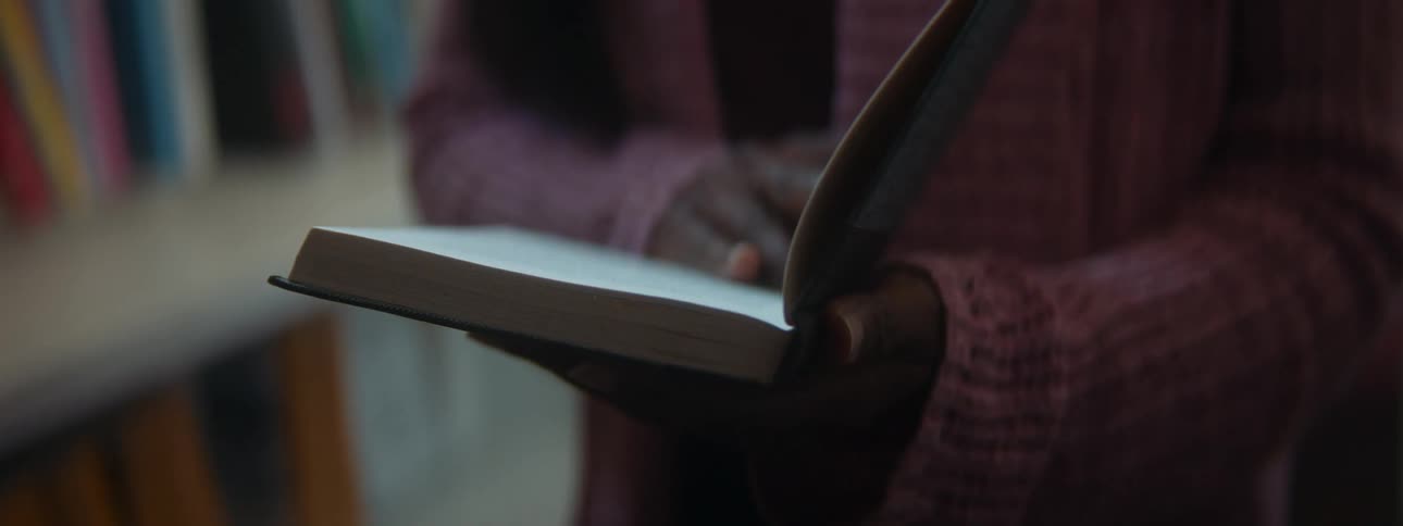 Girl with pink coat turns the pages of book next to bookshelves
