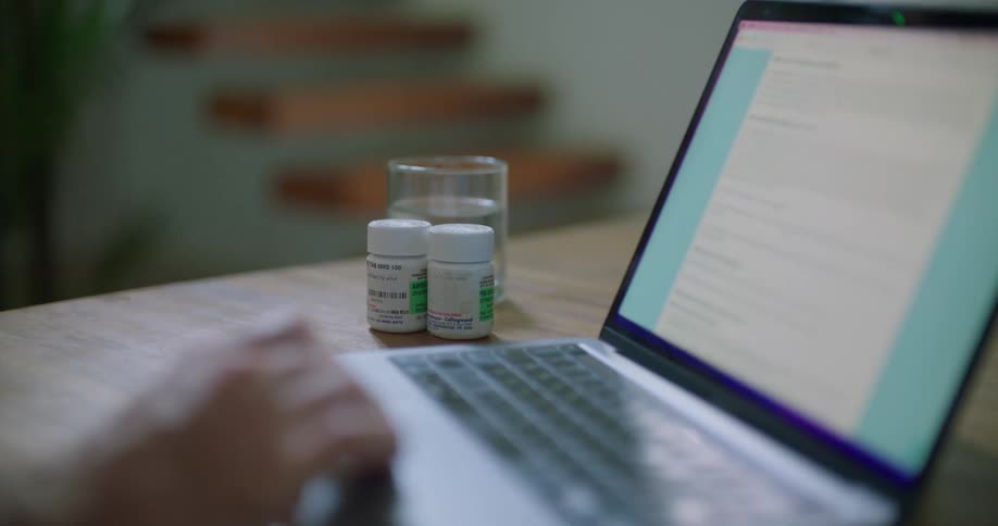 A person scrolls through information on their computer while two prescription bottles sit next to them