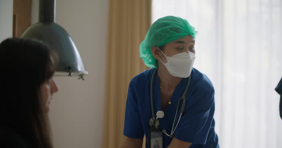 A woman is sitting up in a hospital bed and a nurse puts her stethoscope around her neck as she speaks to the patient