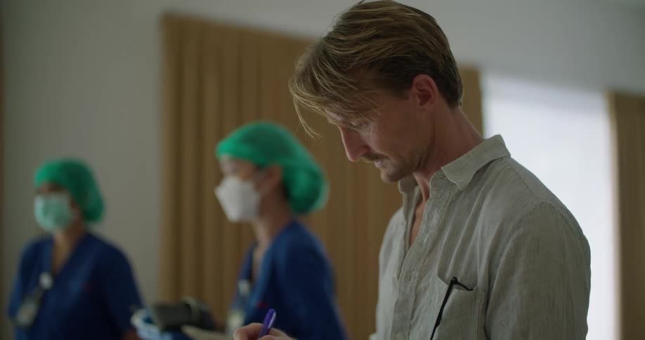 Supervisor standing next to a couple nurses takes notes inside a hospital room