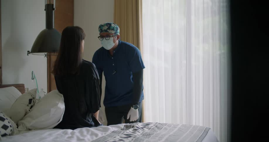 A doctor making a house call examines a woman sitting on her bed