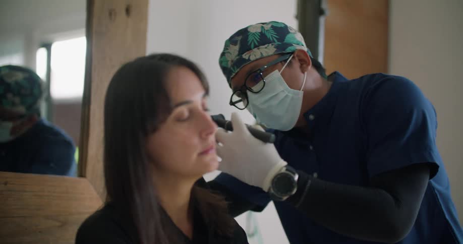 A woman is sitting up in a hospital bed and a doctor is checking her ears with an otoscope