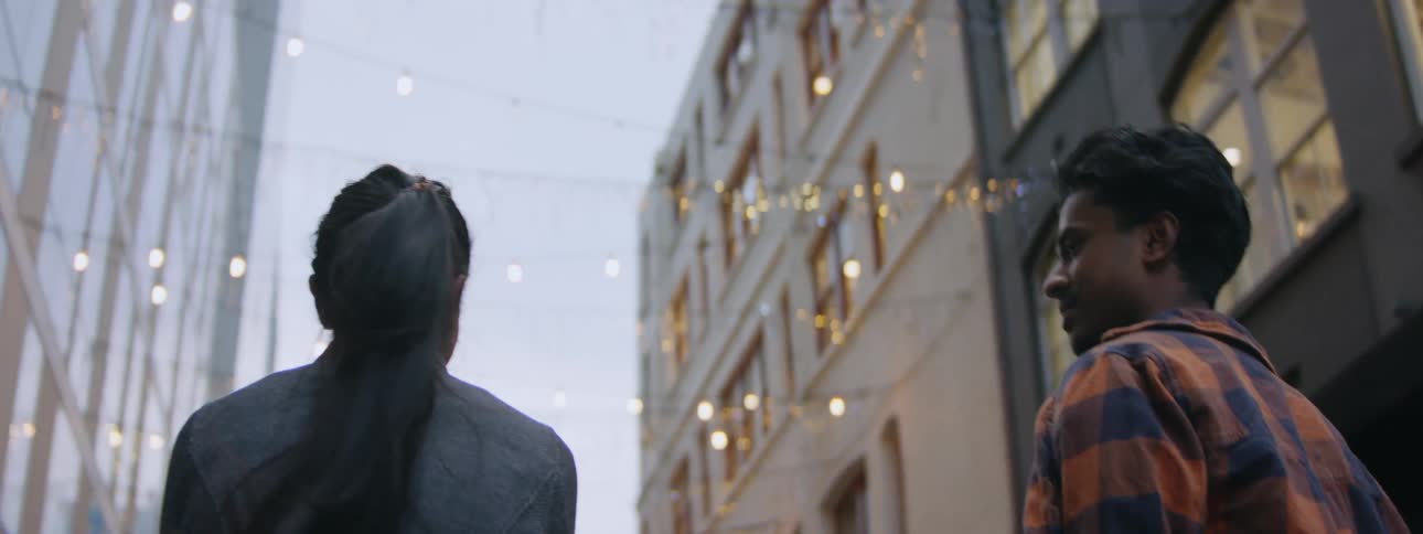 A man and woman walk together along a street lined with tall buildings while happily talking