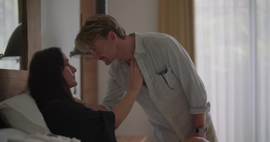 A man says goodbye to a doctor making a house call and then walks over to his wife who is in bed and kisses her