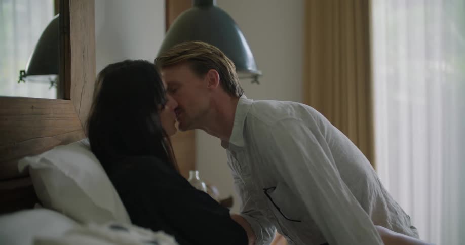A man sitting on a bed kisses his wife who is sitting up in bed
