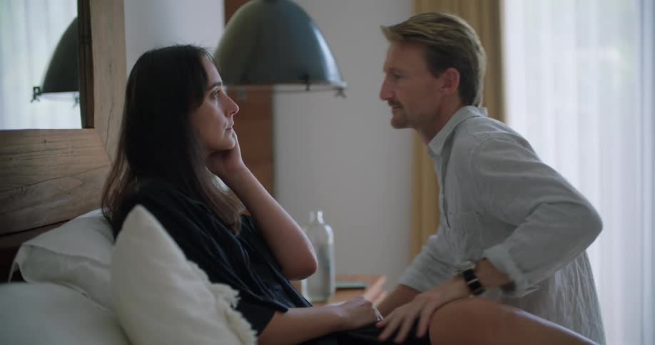 Man with blue shirt and wristwatch attends woman kissing her forehead and sitting on bed