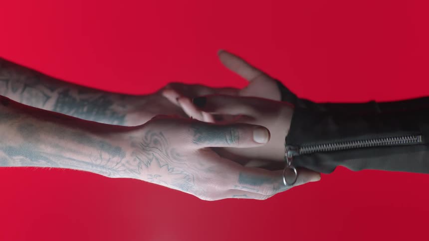 Mans hands with tattoos and womans hands hold each other on the red background
