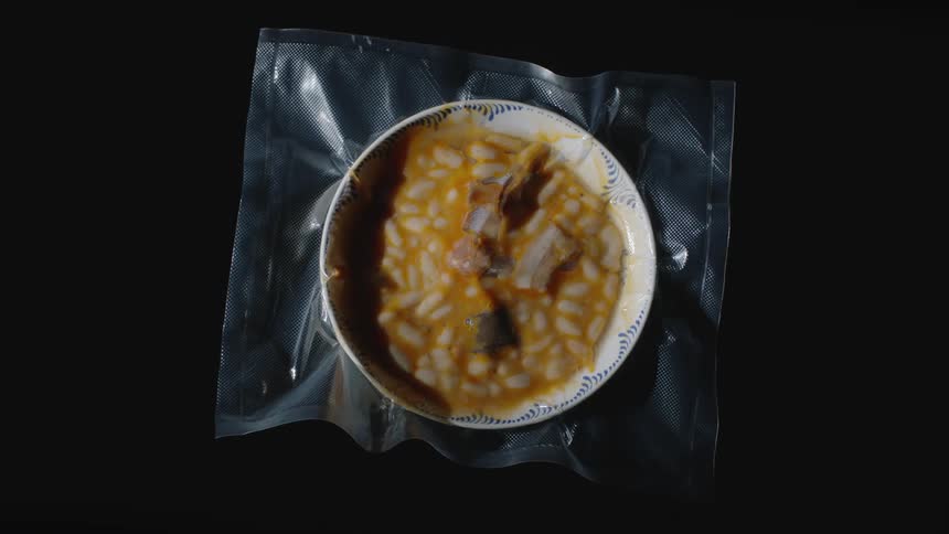 A bowl of hearty soup with plentiful beans sits on a place mat