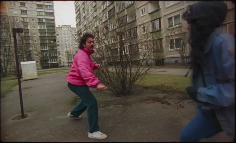 A man and woman play fight with sticks as swords in the courtyard of a large city apartment complex