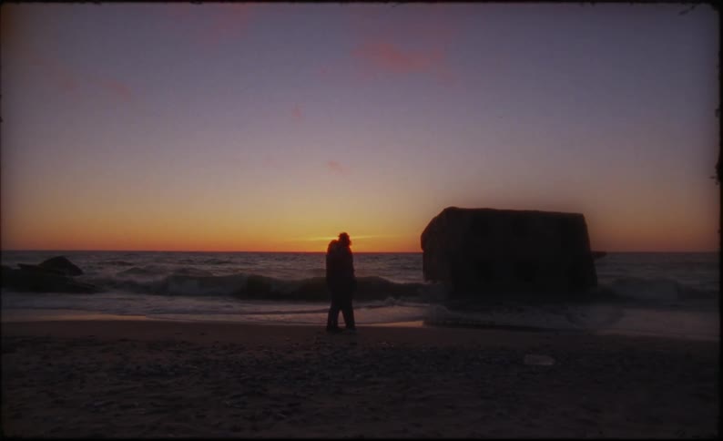 Two people standing out on the beach at sunset