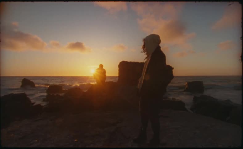 A woman watches on the beach as a man wades in the water