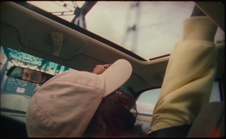 A woman in the passenger seat has her hand out the sunroof as they drive across a bridge