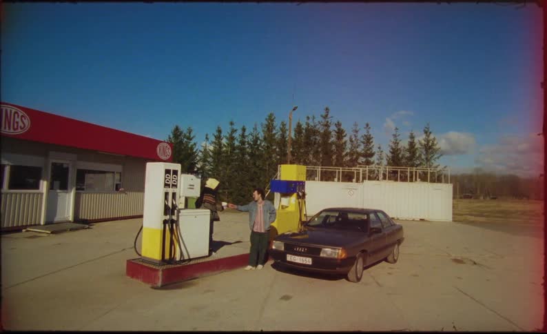 Two people drinking while their car fills up at a gas station