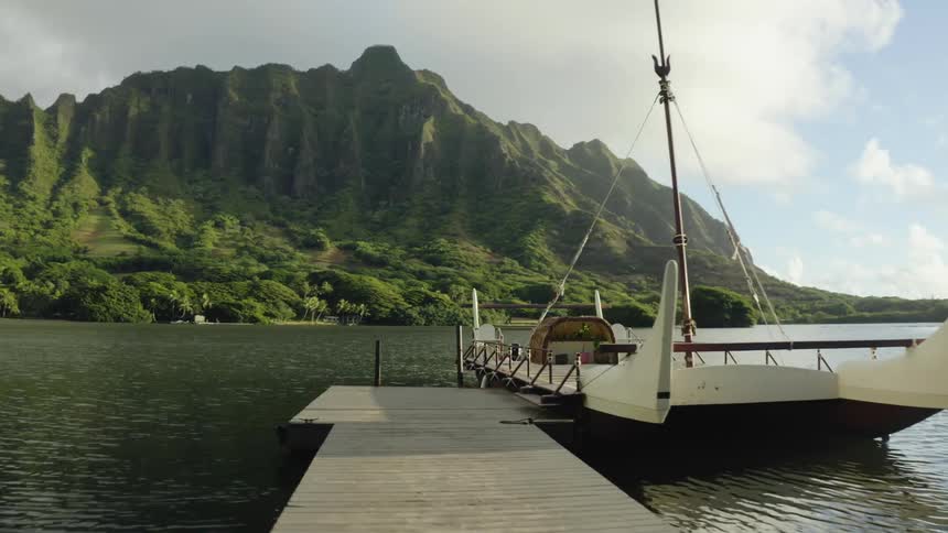 A flat boat docked on a wooden pier across the water from a green mountain