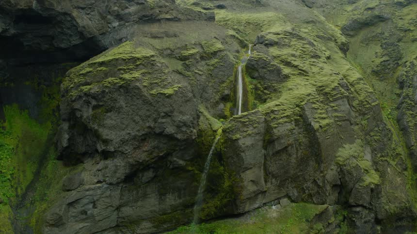 A mountain covered in green plants and moss with flowing waterfalls