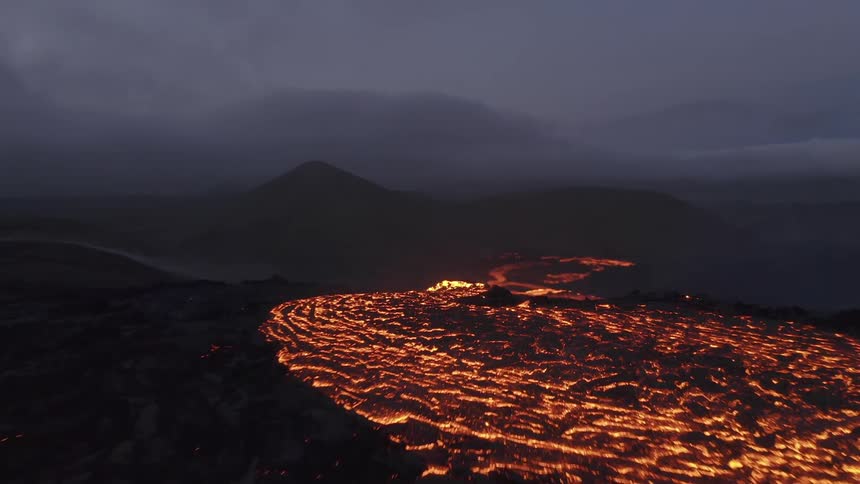 Spilled lava glows bright orange below a volcano