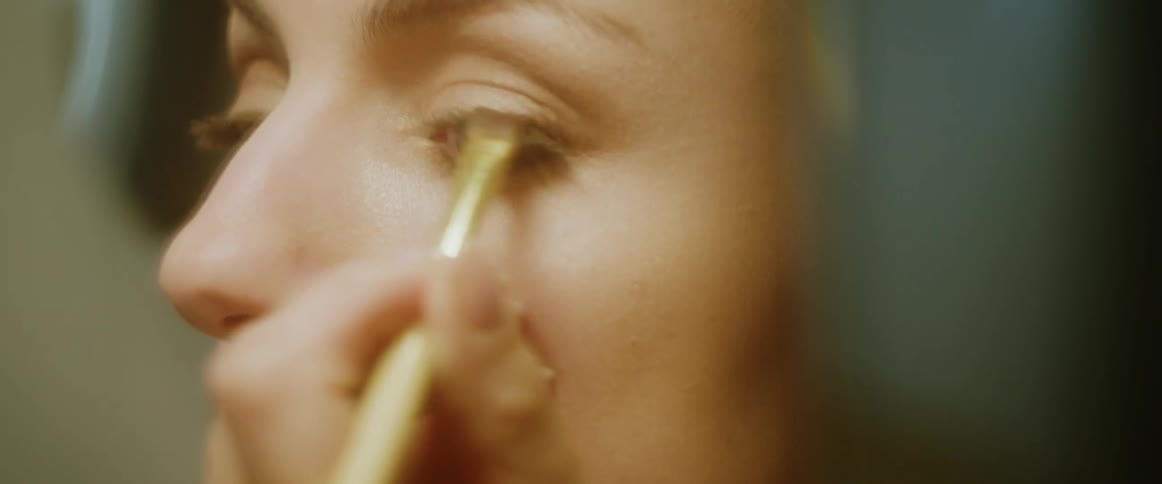 A woman is putting makeup on her eye lid with a makeup brush