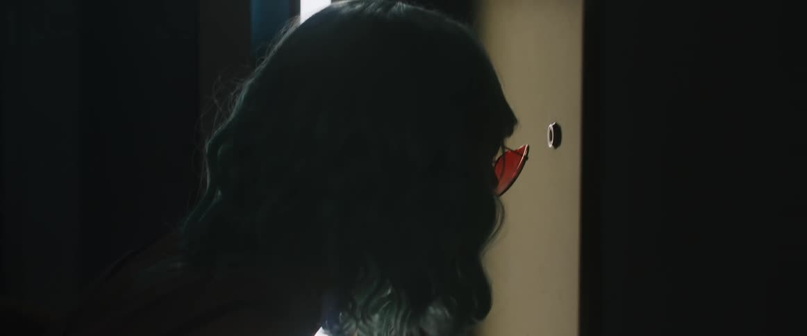 A woman wearing sunglasses looks into the peephole in a door