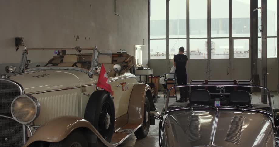 Barber cutting a clients hair inside a garage for vintage antique classic cars