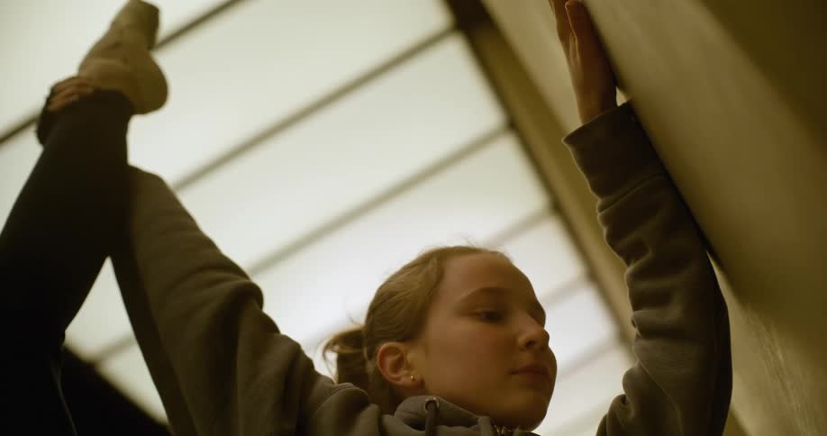 A teenaged ballerina is stretching her leg next to a wall