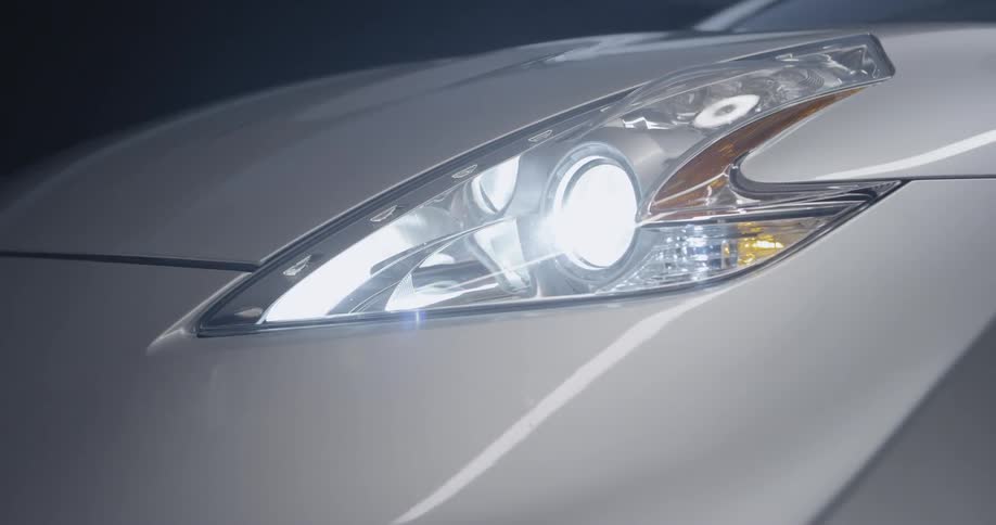 A silver car has a bright headlight
