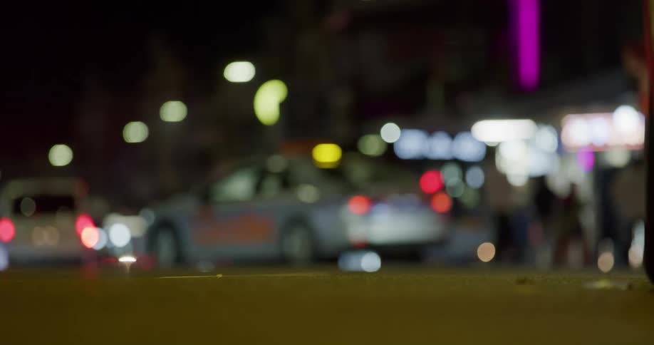 A city street level view of people crossing and cars traveling at night
