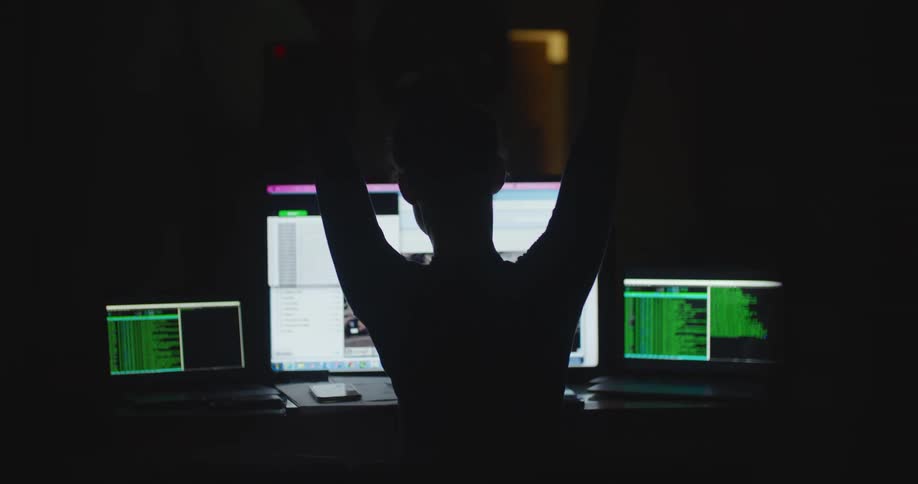 A person in a dark office stretches in front of computer monitors