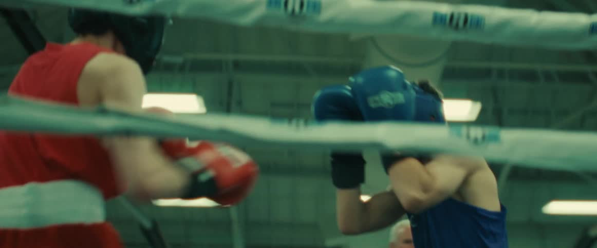 A pair of boxers wearing protective headgear compete in a boxing ring