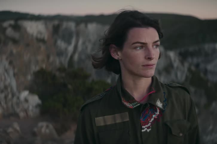 A young white woman is standing outdoors and you can see mountain in the distance