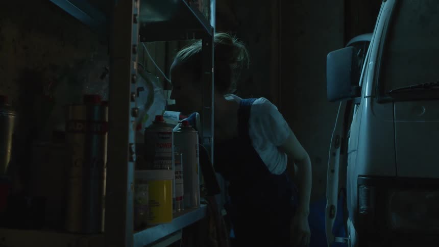 Woman moves between shelves and van looking in a dark garage