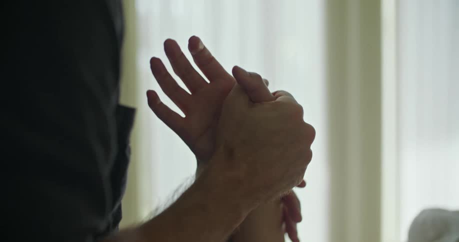 A woman is lying in bed and a man is holding her hand with both of his hands as he kisses her fingers