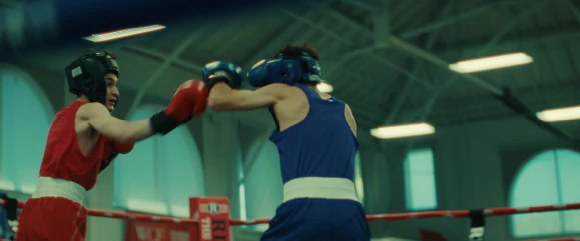A referee watches as two teenage boys throw punches in a boxing ring