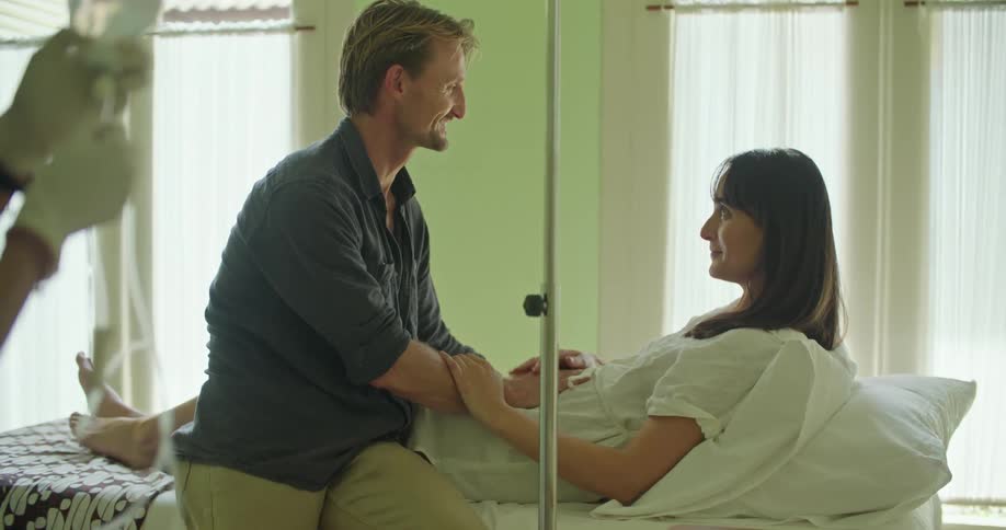 A man comforts his wife while she lies in a hospital bed