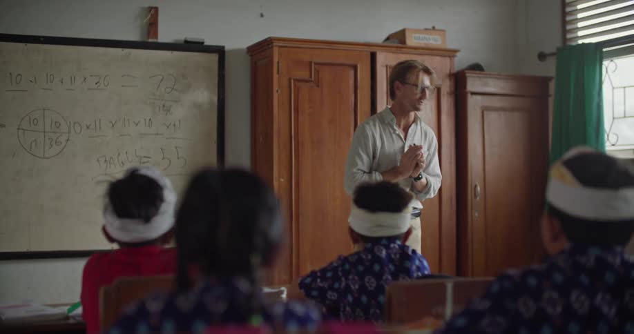 A teacher stands in the front of his classroom while speaking to parents