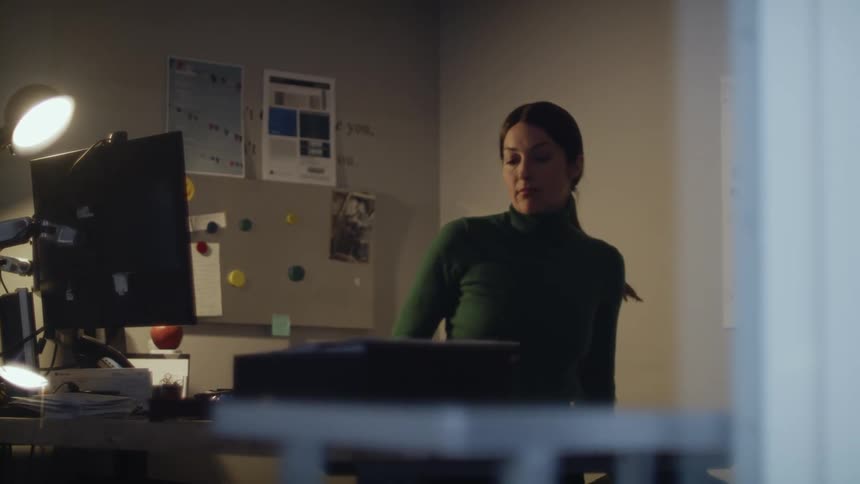 Woman turns on desk lamp and puts down coat before using computer