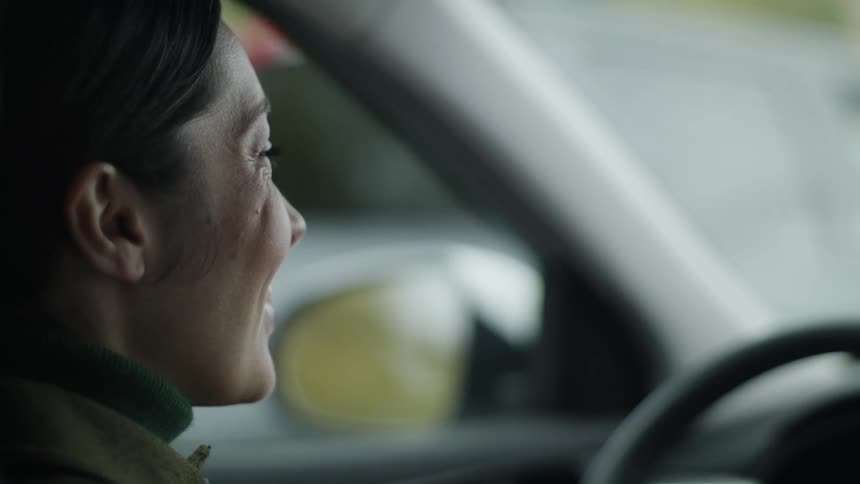 A woman sits behind the steering wheel in her car and smiles and laughs