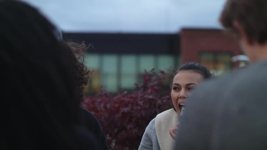 A woman is laughing and smiling as she looks at people around her and puts a fork to her mouth to eat