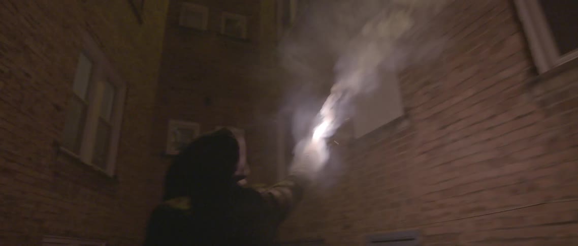 A person waves a flair in an alleyway