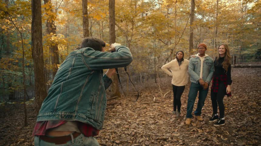 Man takes pictures with a camera of a group of friends standing in the forest at morning