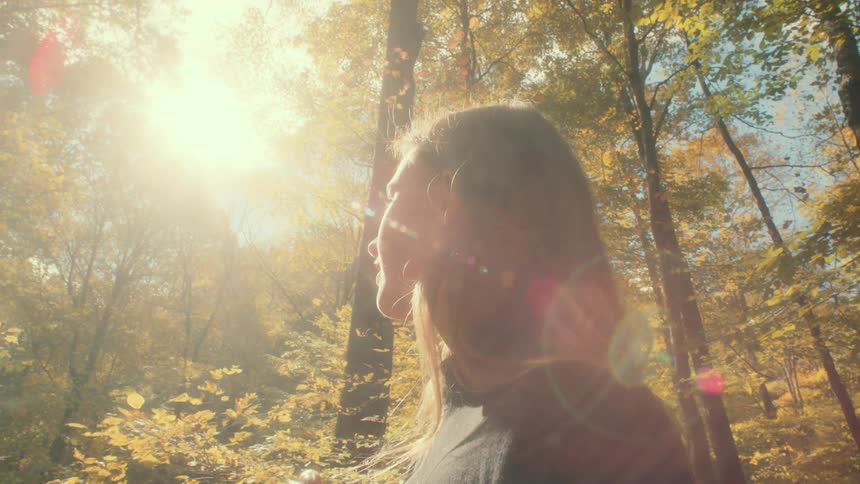 Young woman standing in the forest turns her head up to face the bright sun