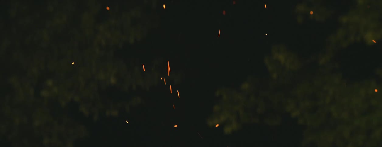Bright yellow sparks from a campfire floating up in the air at night