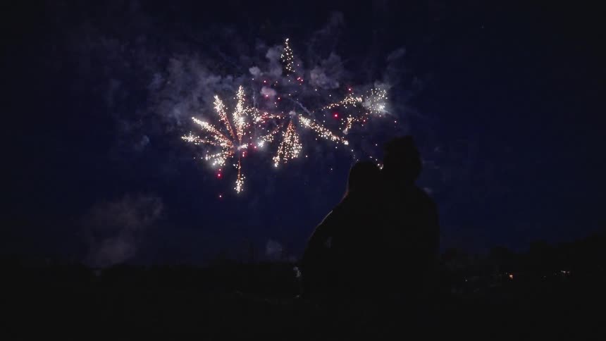 The silhouette of two people sitting close together watching fireworks burst and explode in the sky