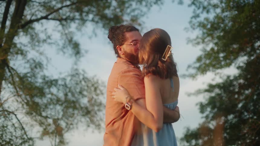 A man and woman hug and kiss under trees
